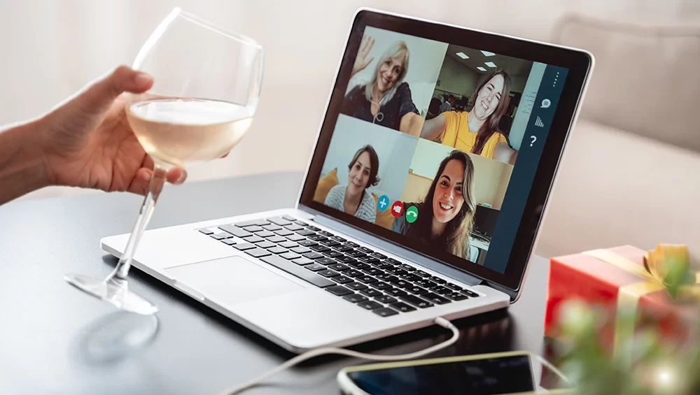 Happy Woman Celebrating On Christmas Virtual Video Call Party Cheering With Wine Online At Home 1000x565