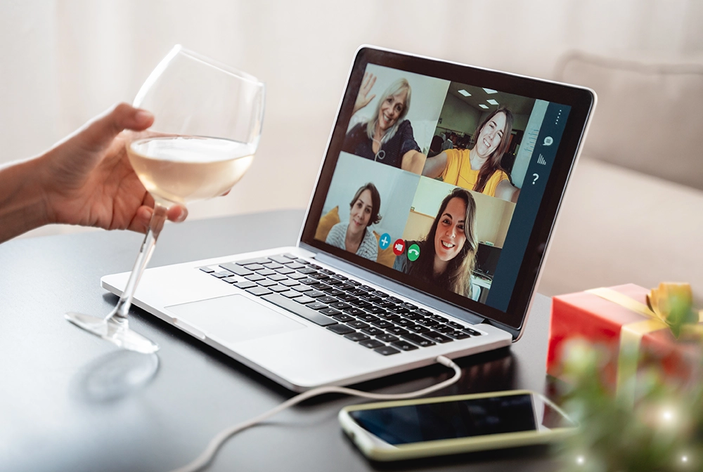 Happy woman celebrating on Christmas virtual video call party cheering with wine online at home